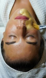 A woman enjoying a gold facial mask for relaxation and skincare at a spa.