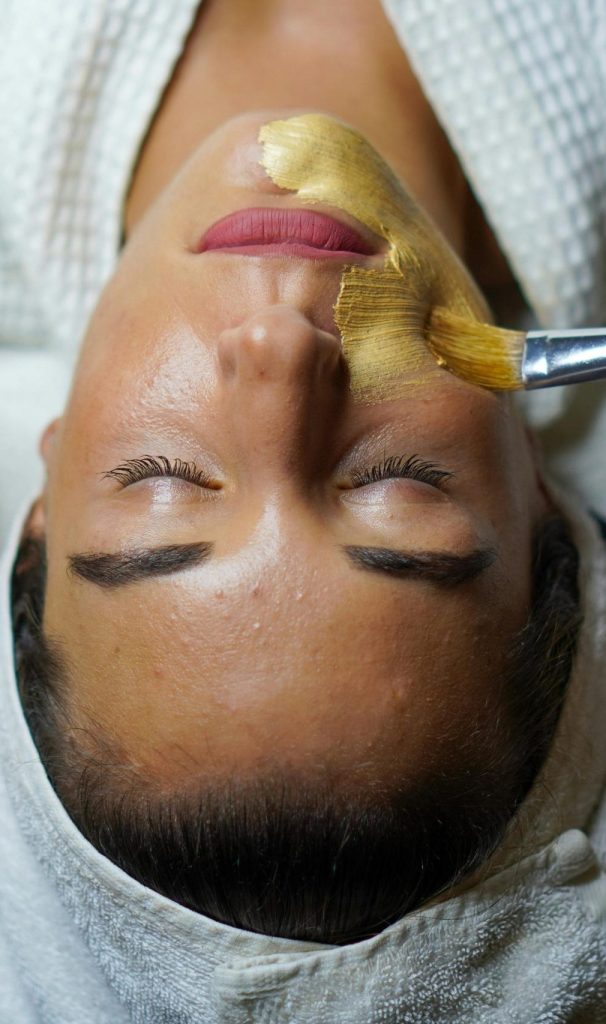 A woman enjoying a gold facial mask for relaxation and skincare at a spa.