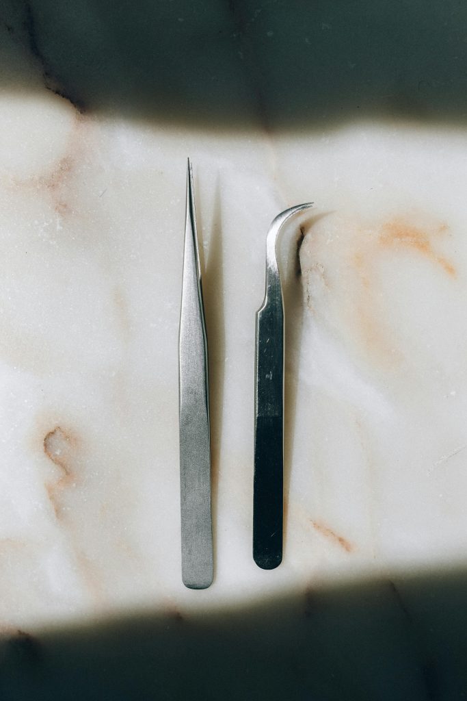 Close-up of sharp metal tweezers on a marble surface, highlighting textures and shadows.